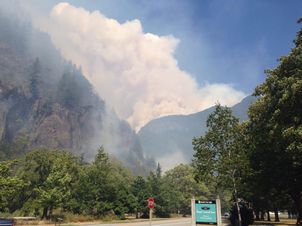 Seattle City Light’s company town of Newhalem and Highway 20 in the foreground with smoke from the Goodell Creek Fire on the steep terrain in the background.